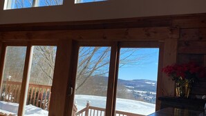 A room with large windows, a wooden deck, and a view of a snowy landscape.