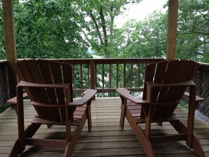 Zwei Holz-Adirondack-Stühle auf einer Holzterrasse mit Blick auf Bäume.