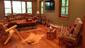 Uma sala de estar aconchegante com um sofá, poltronas, uma mesa de centro de madeira e um urso de pelúcia grande no chão.