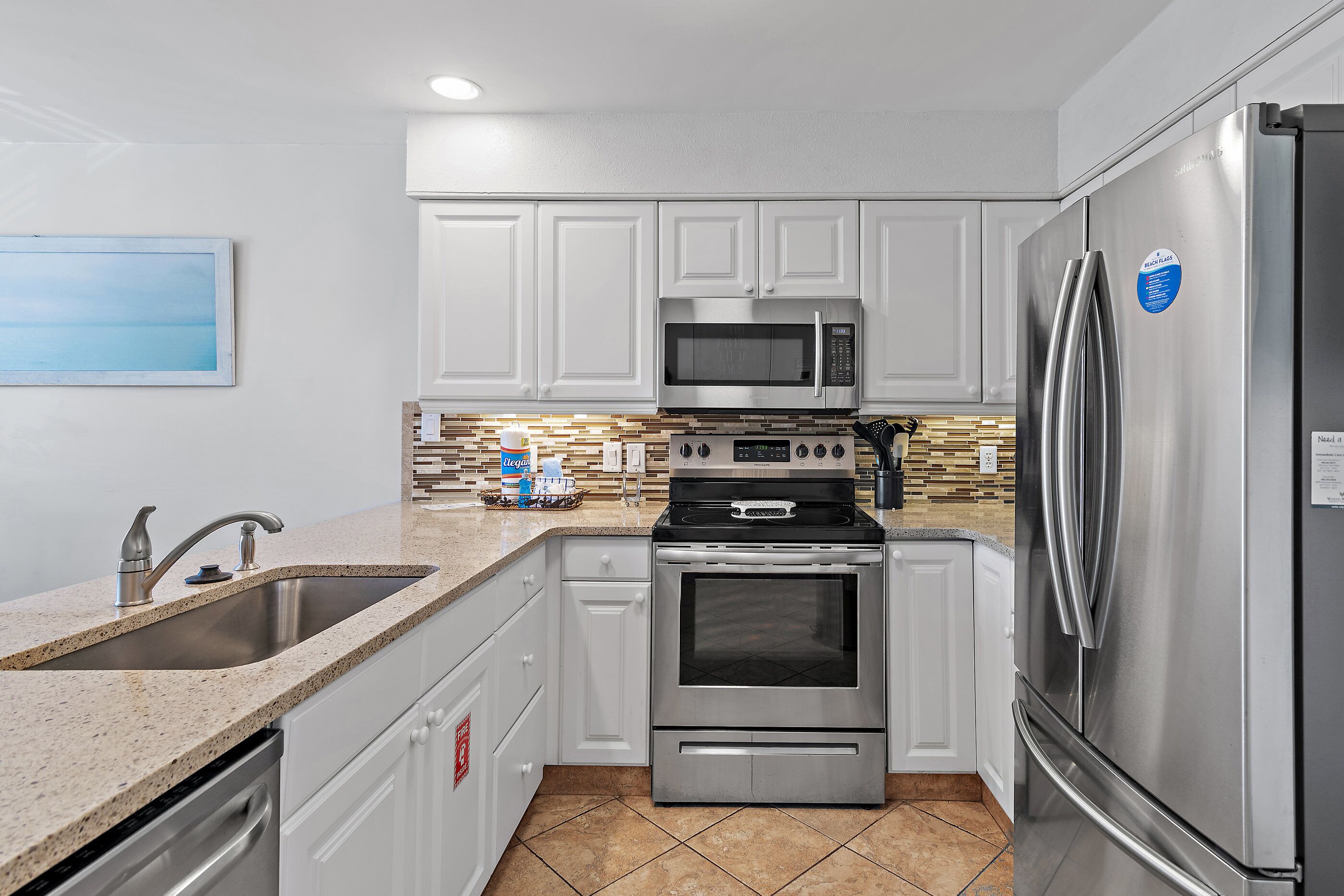 A kitchen with white cabinets, stainless steel appliances, a granite countertop, and a tiled backsplash.