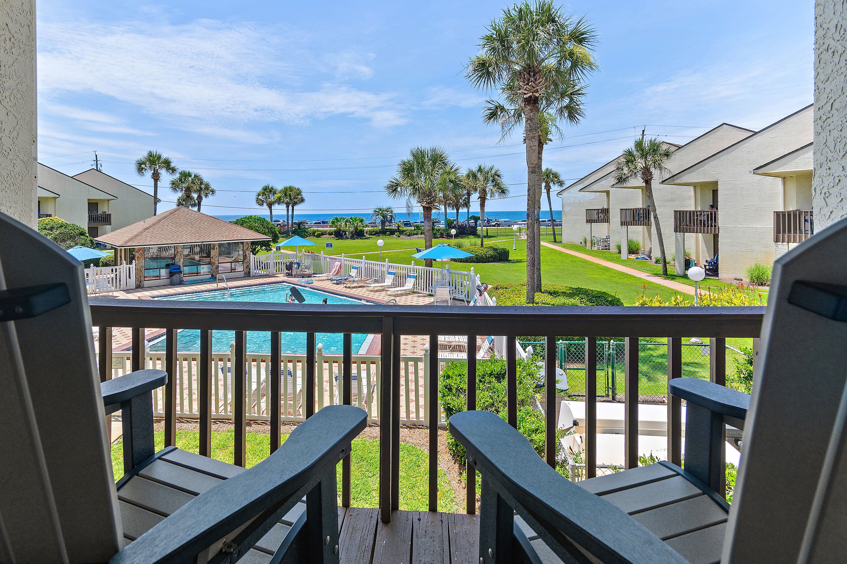Ein Balkon mit Blick auf ein Schwimmbad, Palmen und einen Strand.