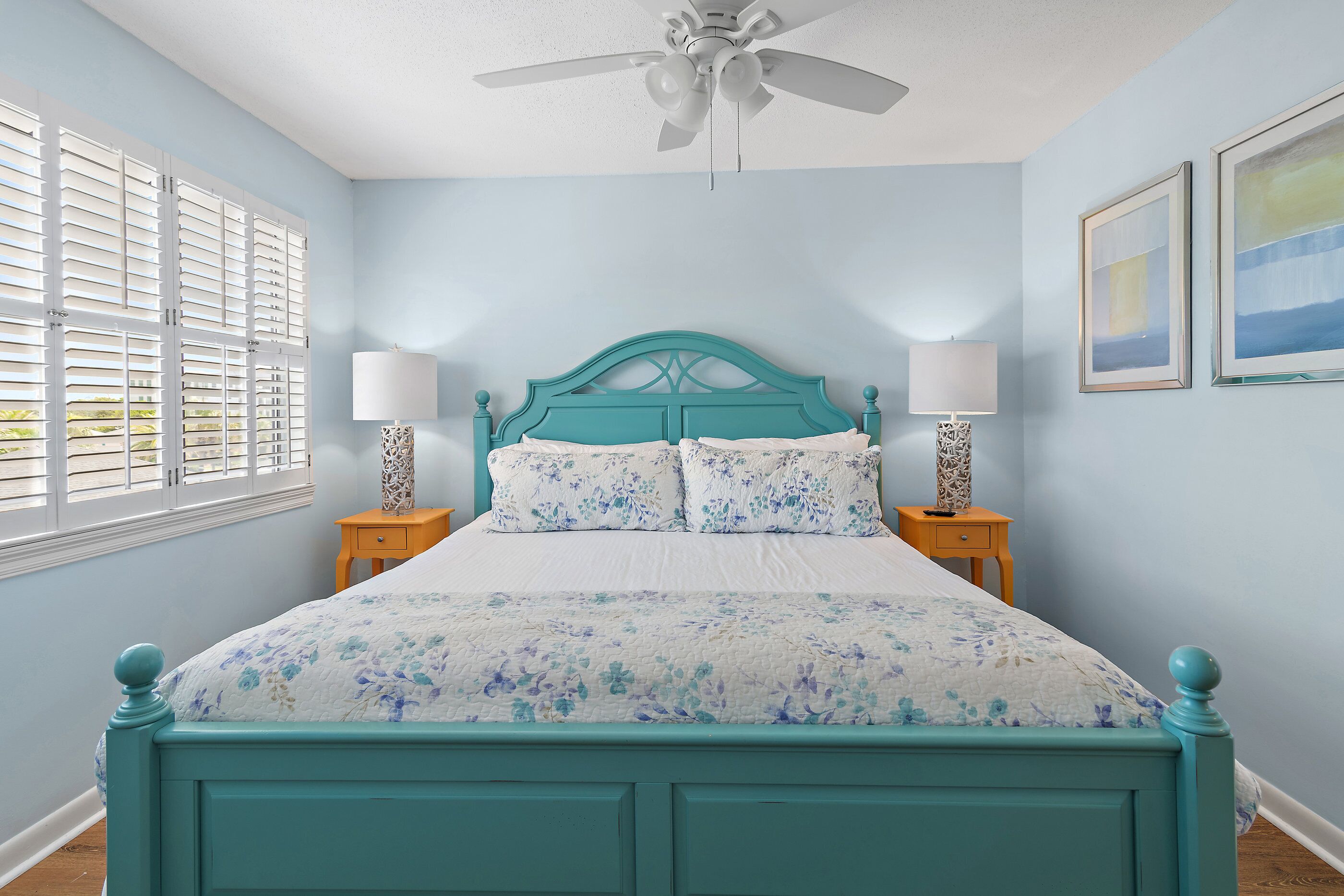 A bedroom with a teal bed, white bedding, two bedside lamps, and a ceiling fan.