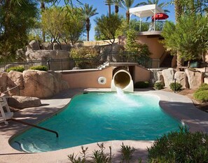 Relax by the pool surrounded by lush greenery and natural rock formations, featuring a fun water slide.
