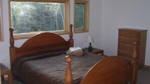 A bedroom with a wooden bed, a nightstand, a dresser, and a window with a view of trees.