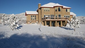A large, two-story house with a balcony, surrounded by snow-covered ground and trees. - 6000 sq ft Estate Home on 3 Acres near USAFA in the Rockies (Monument)