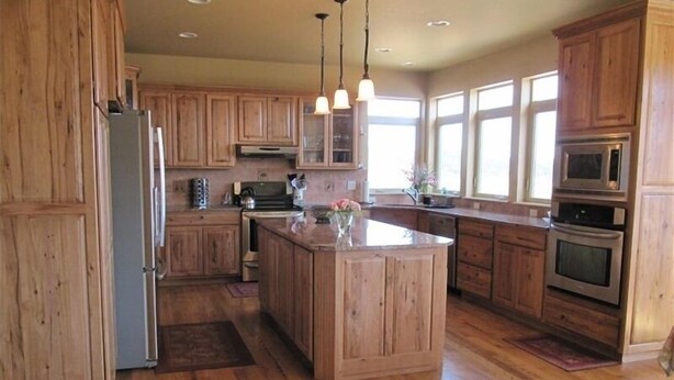A spacious kitchen with wooden cabinets, a central island, stainless steel appliances, and large windows providing natural light. - 6000 sq ft Estate Home on 3 Acres near USAFA in the Rockies (Monument)