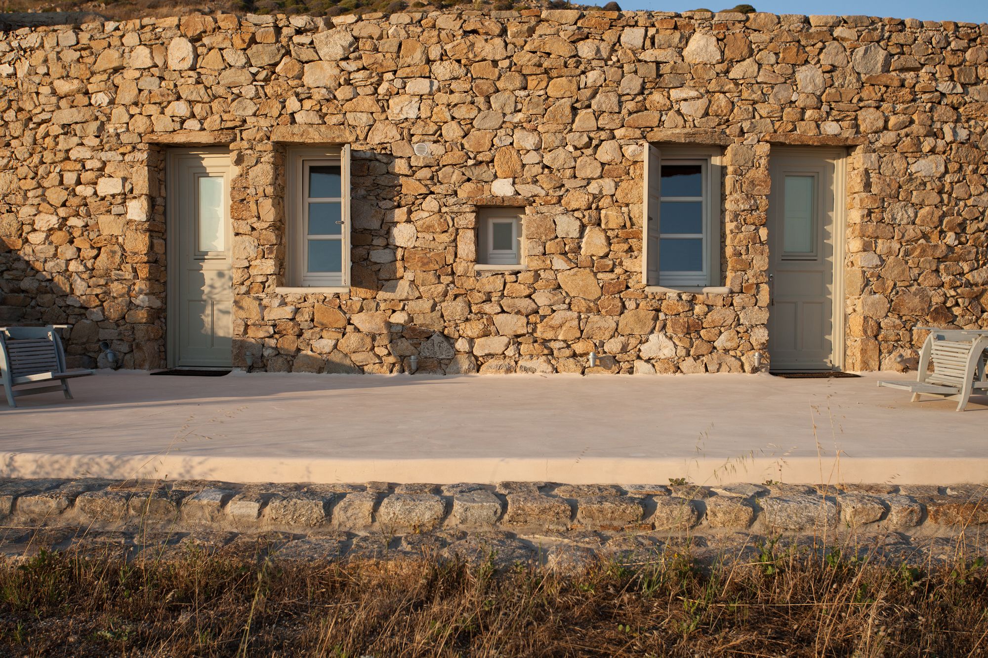 A stone building with two doors and windows, a paved entrance, and outdoor seating.