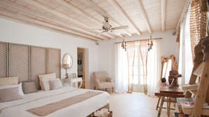 Quarto com cama grande, uma cadeira, escrivaninha e ventoinha no teto.