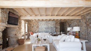 Um quarto rústico com paredes de pedra, um sofá branco, uma mesa de madeira e uma lareira de pedra.