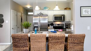 A modern kitchen with white cabinets, stainless steel appliances, and a central island with wicker chairs.