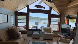 A cozy living room with a large window overlooking a lake, a television, and a ceiling fan. - Glen Lake  - Spectacular Dune Views & Complete Privacy! (Glen Arbor)