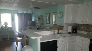 Une cuisine compacte avec des meubles blancs, un lave-vaisselle, un évier et un coin repas comprenant des chaises et une table.