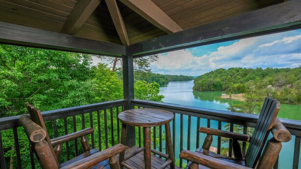 Una terraza de madera con dos sillas y una mesita, con vistas a un río y abundante vegetación.