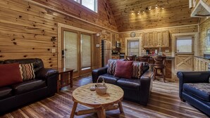 Un interior de cabaña acogedor con paredes de madera, una sala de estar con sofás de cuero, un comedor y una cocina con armarios de madera.