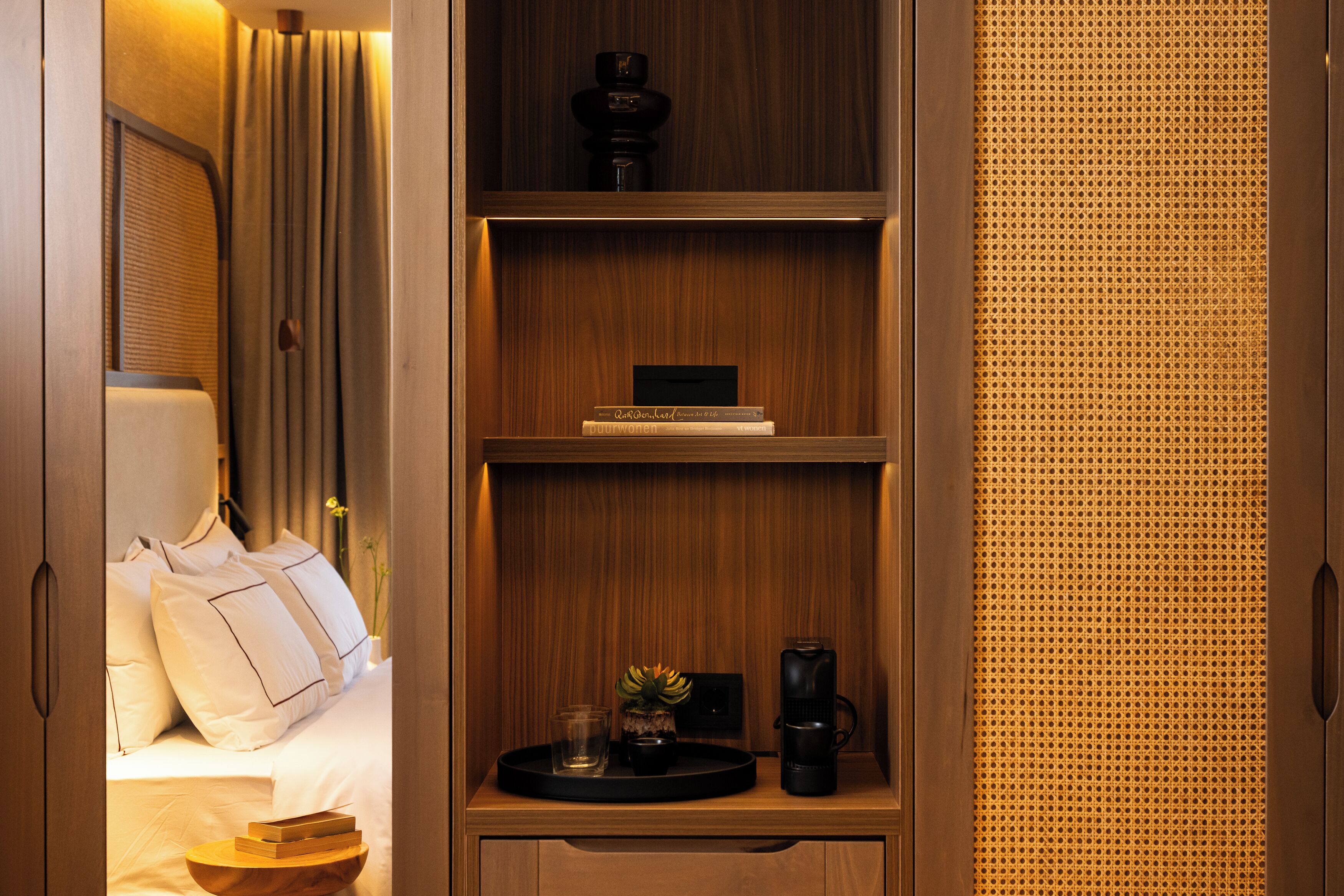 A hotel room with a wooden wardrobe, a bed with white linens, a small table with a tray, and a window with curtains.