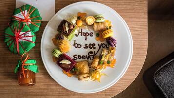 A plate of assorted pastries and chocolates with a message "Hope to see you soon" on a wooden table.