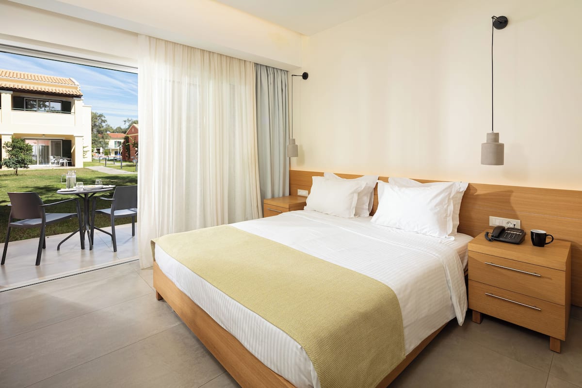 A hotel room with a large bed, bedside tables, a desk with chairs, and a view of the outdoor area.