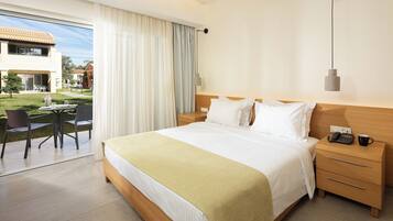 A hotel room with a large bed, bedside tables, a desk with chairs, and a view of the outdoor area.