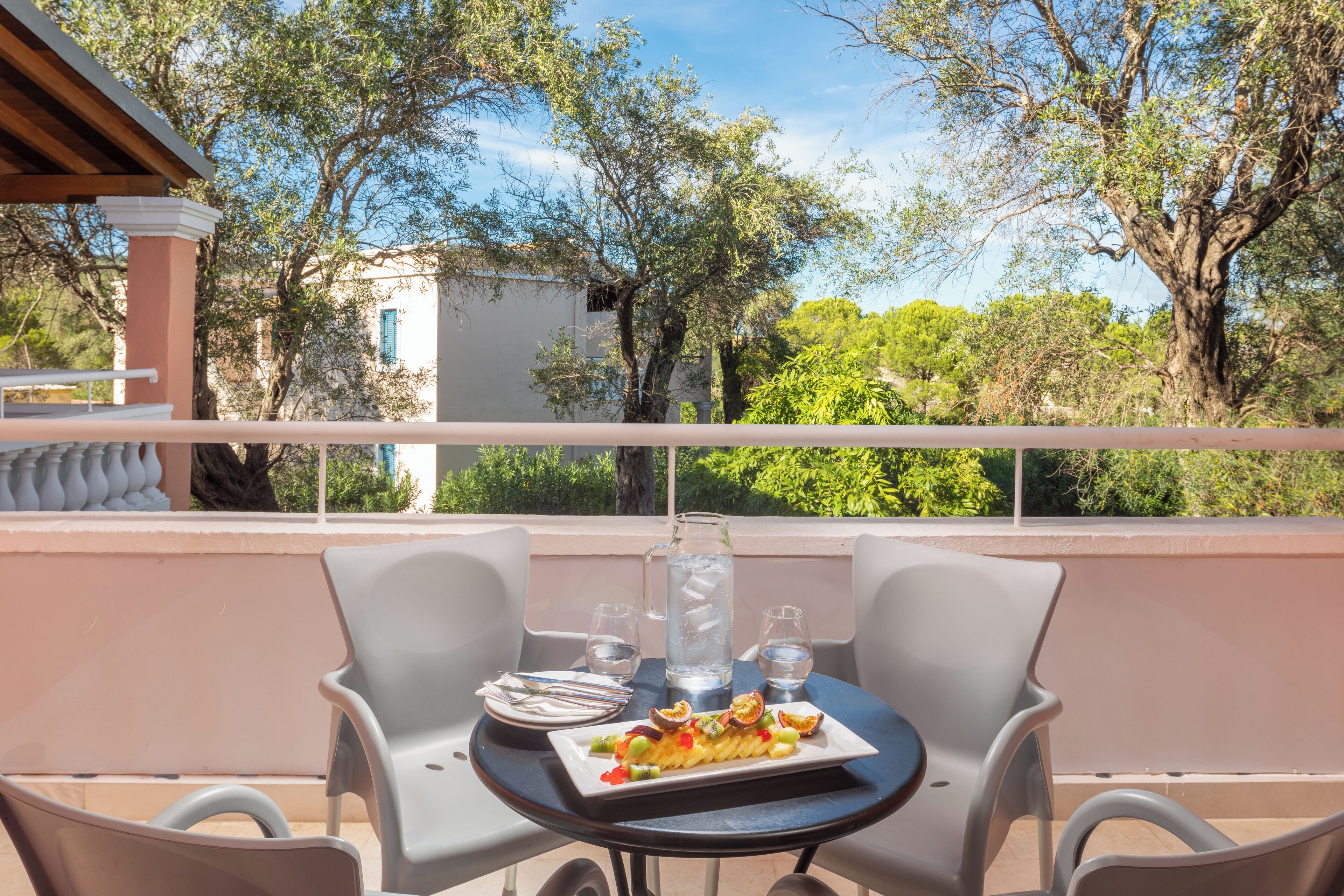 A balcony with a table set for two, featuring a plate of food, two glasses, and a pitcher of water.