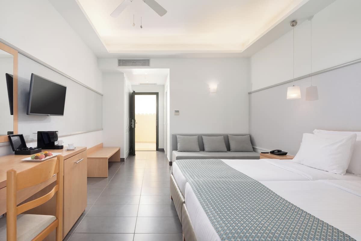 A hotel room with a bed, a desk with a computer, a TV, and a bedside table with a phone.