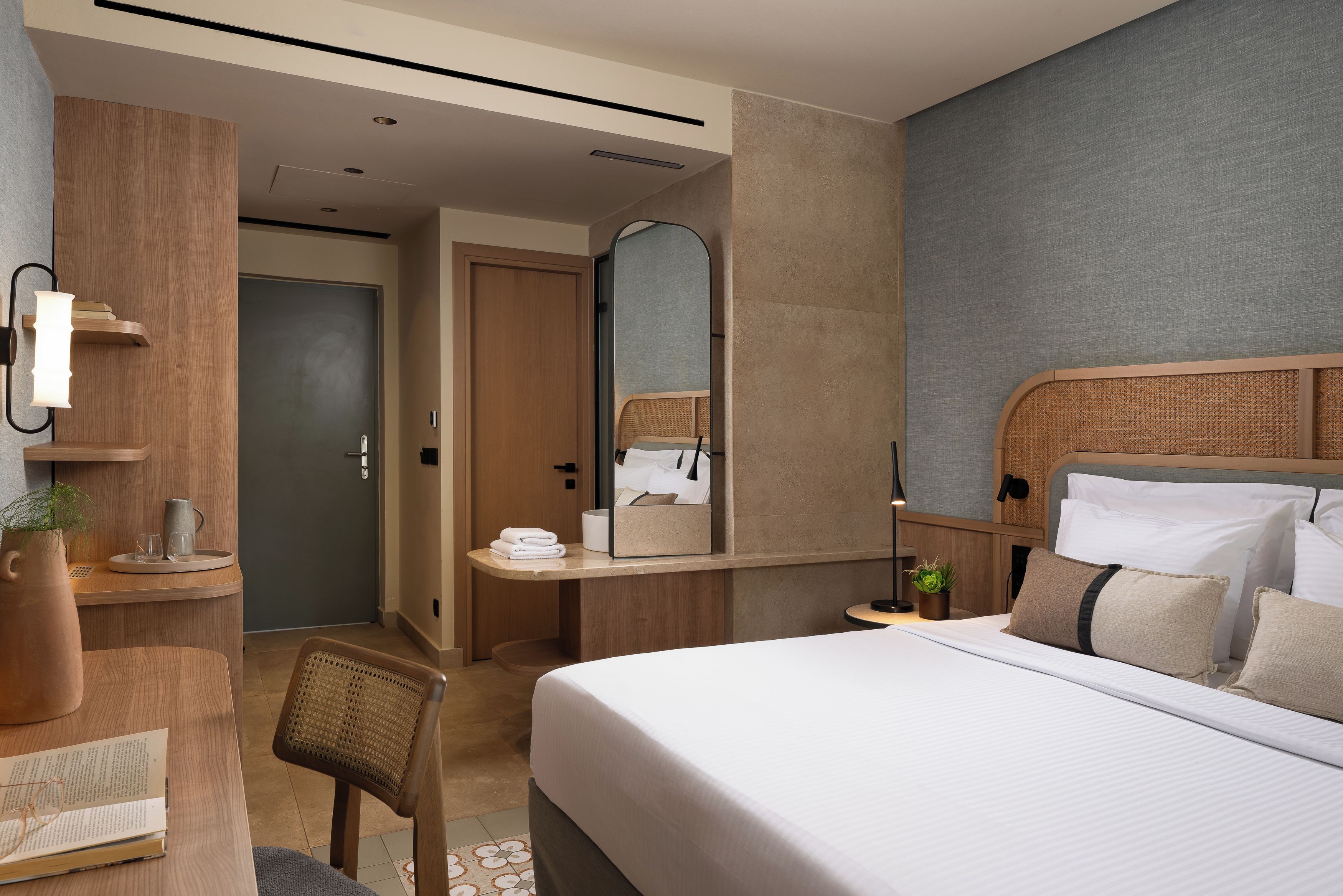 Una habitación de hotel con cama, mesita de noche, espejo y escritorio con silla.