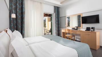 Ein Hotelzimmer mit zwei Betten, einem Schreibtisch, einem Stuhl, einem Fernseher und einem großen Fenster mit Vorhängen.