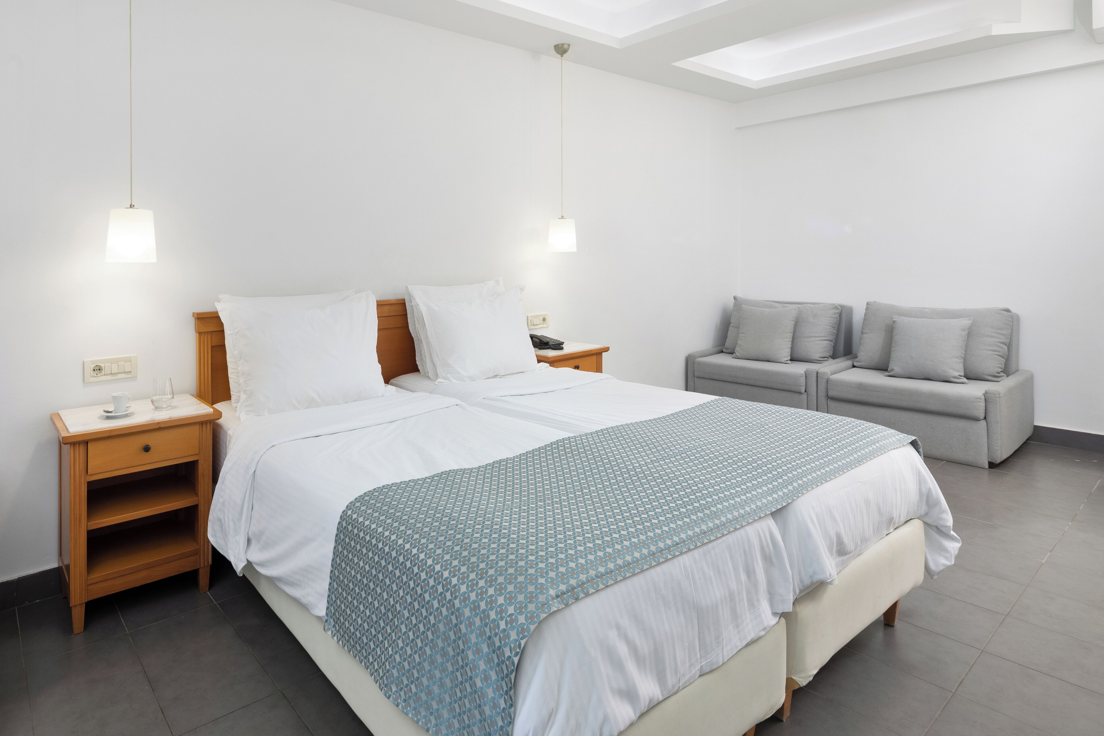 Et moderne hotelværelse med en stor seng, en grå sofa og et lille bord med en lampe.
