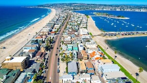 Vista aérea de uma cidade costeira com uma avenida principal, imóveis à beira-mar e um porto de iates.
