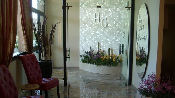A reception area with a marble floor, red upholstered chairs, a potted plant, and a wall with 'HG' letters. - Hotel Giannina (Forlimpopoli)