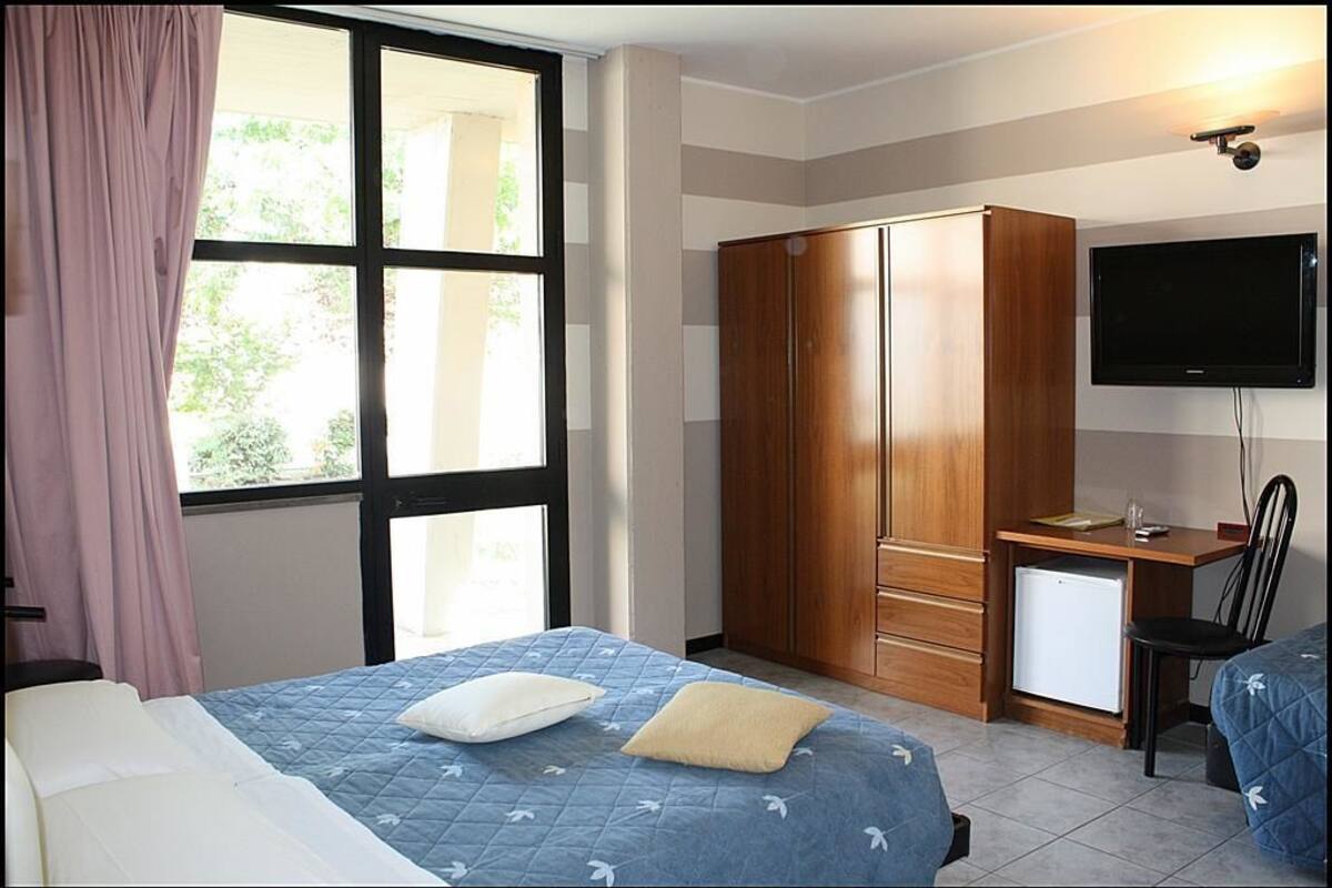 A bedroom with a bed, a wardrobe, a desk with a computer, and a television.