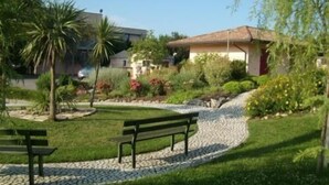 A garden with a paved path, a bench, and a building with a tiled roof. - Hotel Giannina (Forlimpopoli)