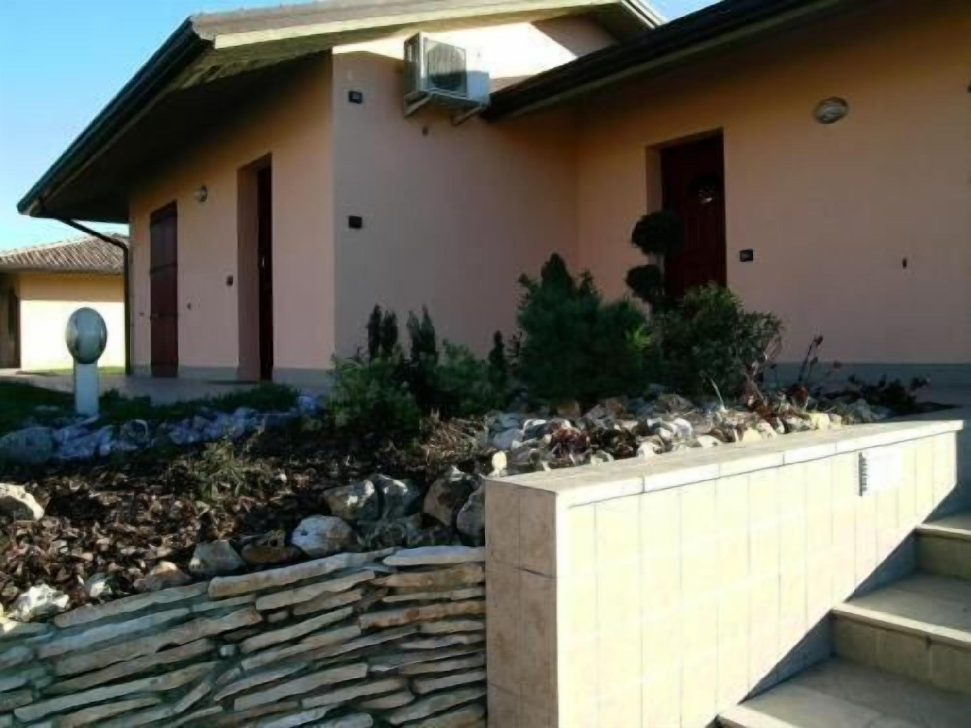 Un edificio con un muro di sostegno in pietra, un piccolo giardino con arbusti e una scala che conduce all'ingresso.