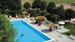 A swimming pool with lounge chairs and umbrellas, surrounded by trees and a grassy area. - Hotel Giannina (Forlimpopoli)