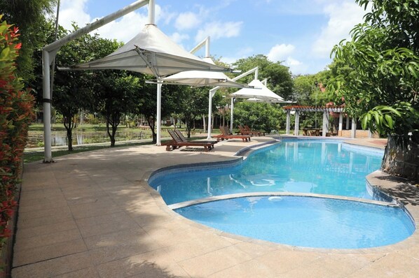 A swimming pool with lounge chairs and umbrellas, surrounded by greenery. - Avasta Resort (Anuradhapura)