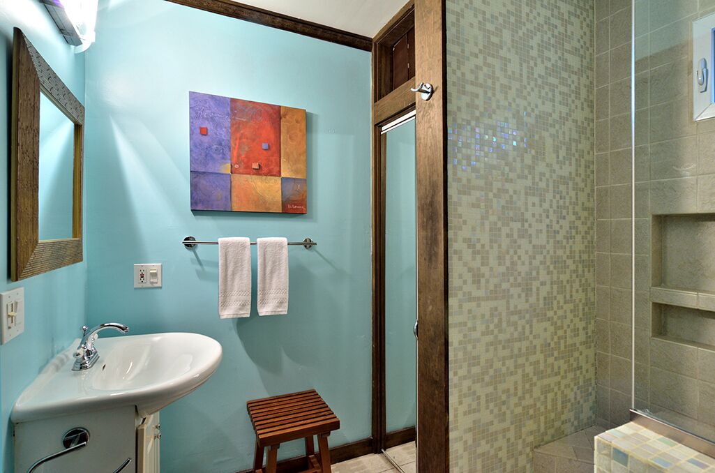 Ein Badezimmer mit Waschbecken, zwei Handtüchern, einem Holzschemel und einer Dusche mit Mosaikfliesen.