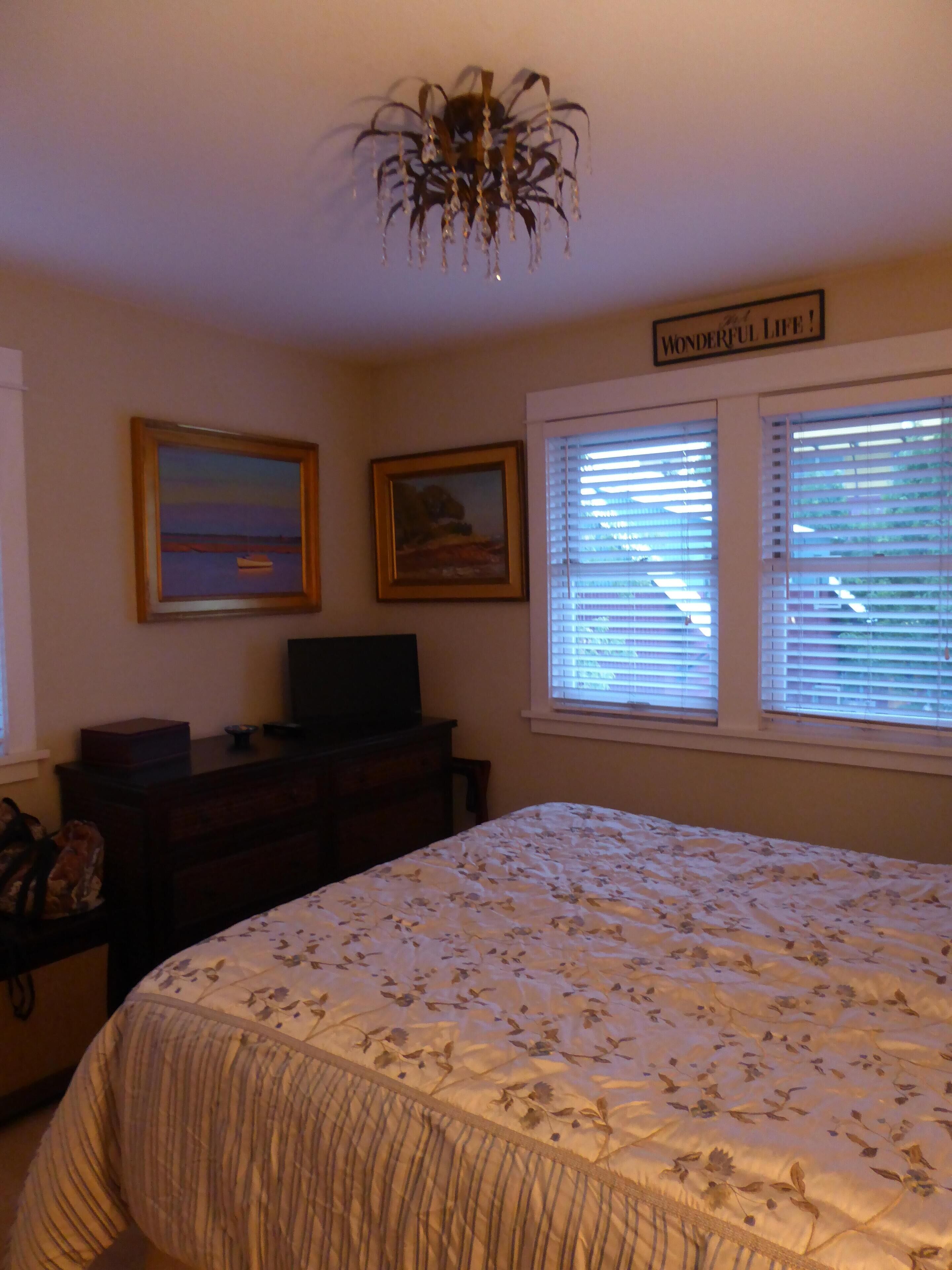 A bedroom with a bed, a dresser, a television, two framed pictures, and a window with blinds.