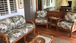 Uma sala de estar com um sofá, duas poltronas, uma mesa de centro e uma mesinha lateral. Há quadros nas paredes e uma pintura sobre a mesa de centro.