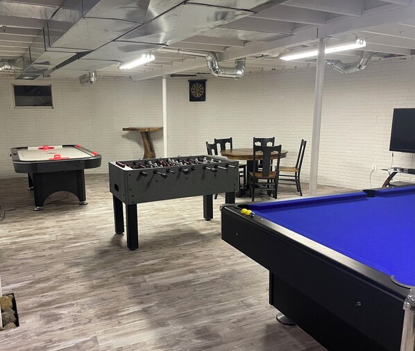 A room with a foosball table, a pool table, a dartboard, and a table tennis table.