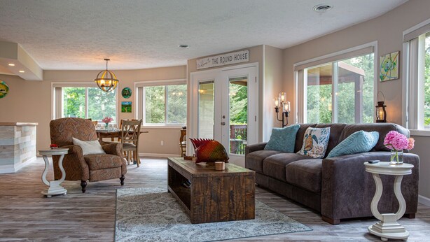 A spacious living room with a large window, a cozy fireplace, and a welcoming sign. - The Round House at Pleasant Hill, Near Mohican & Snow Trails (Perrysville)