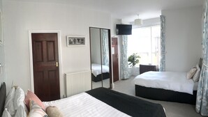 A bedroom with two beds, a large mirror, a TV, and a window with curtains. - Doriam (Bridlington)