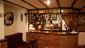 A bar area with a brick wall, wooden bar counter, stools, and a round table. - Doriam (Bridlington)
