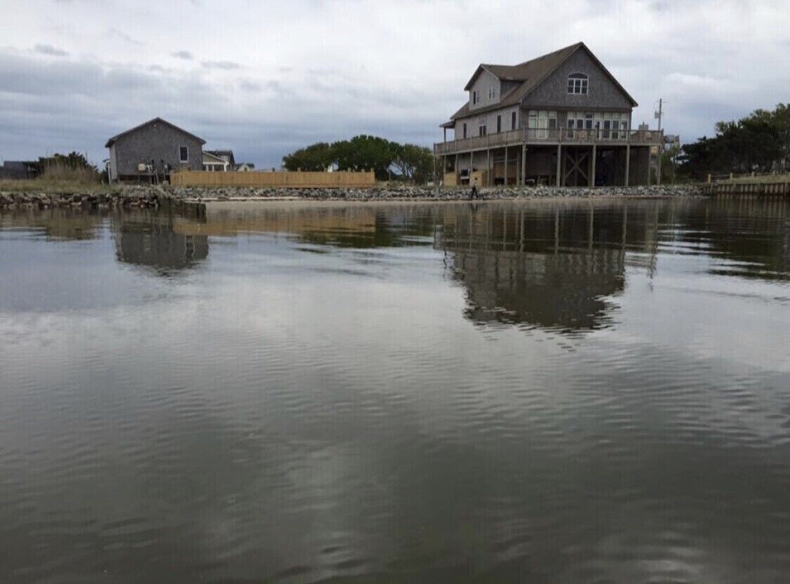 Une propriété située au bord de l’eau, comprenant une grande maison dotée d’un balcon et un bâtiment plus petit à proximité.