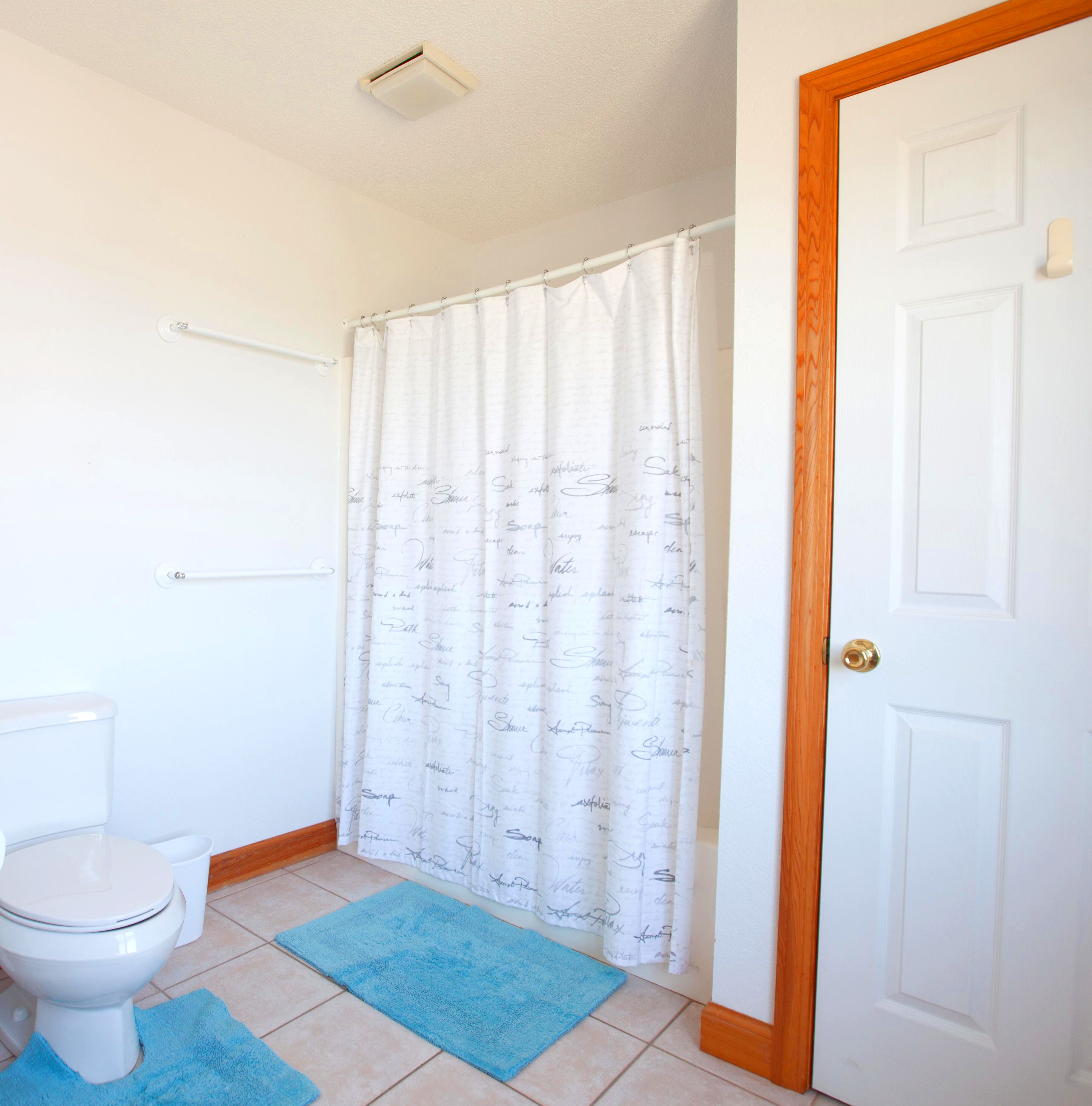 Un baño con inodoro, cortina de ducha con texto escrito a mano y una alfombra de baño azul.