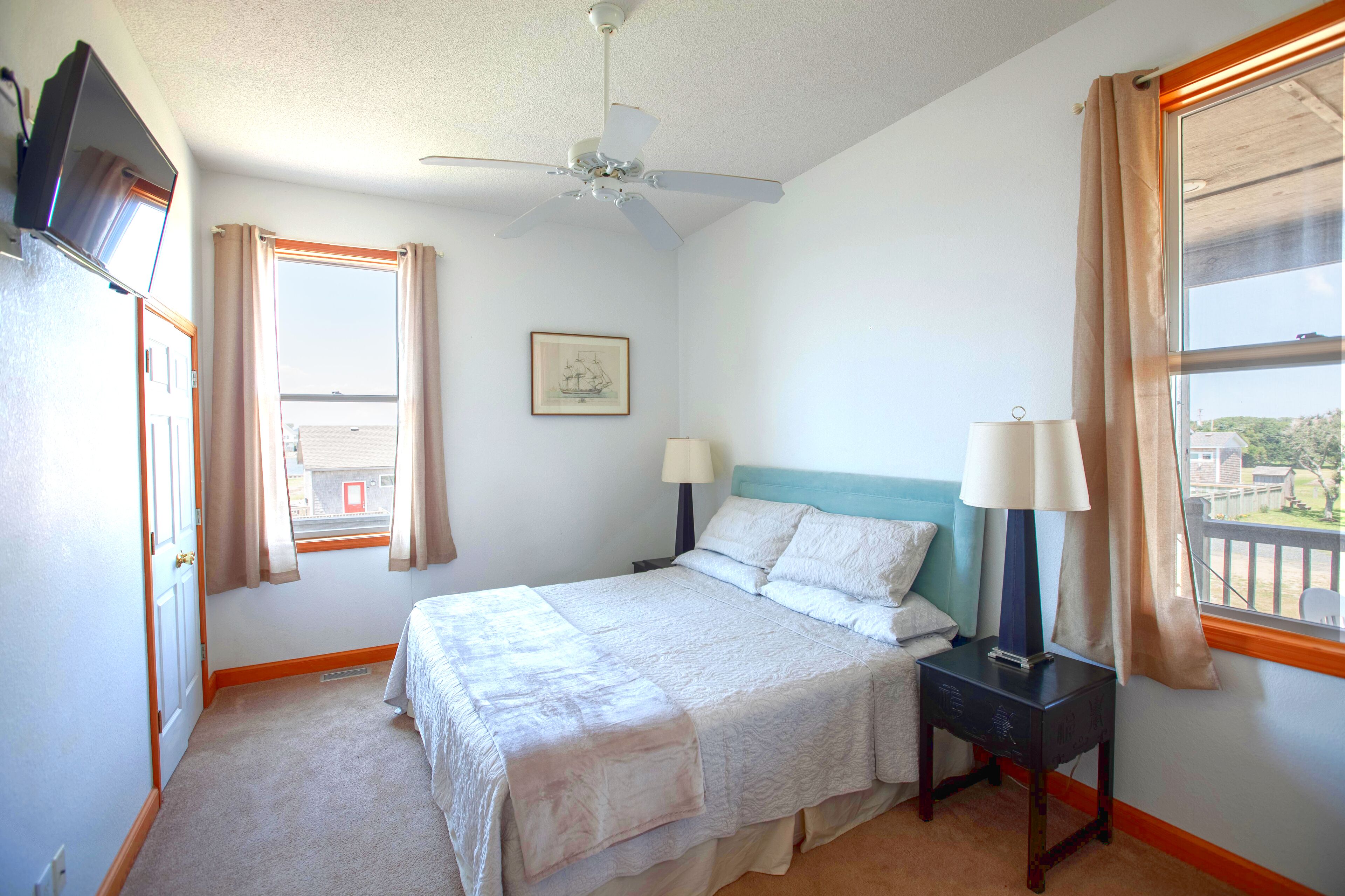 A bedroom with a bed, two bedside lamps, a ceiling fan, a window with curtains, and a framed picture on the wall.
