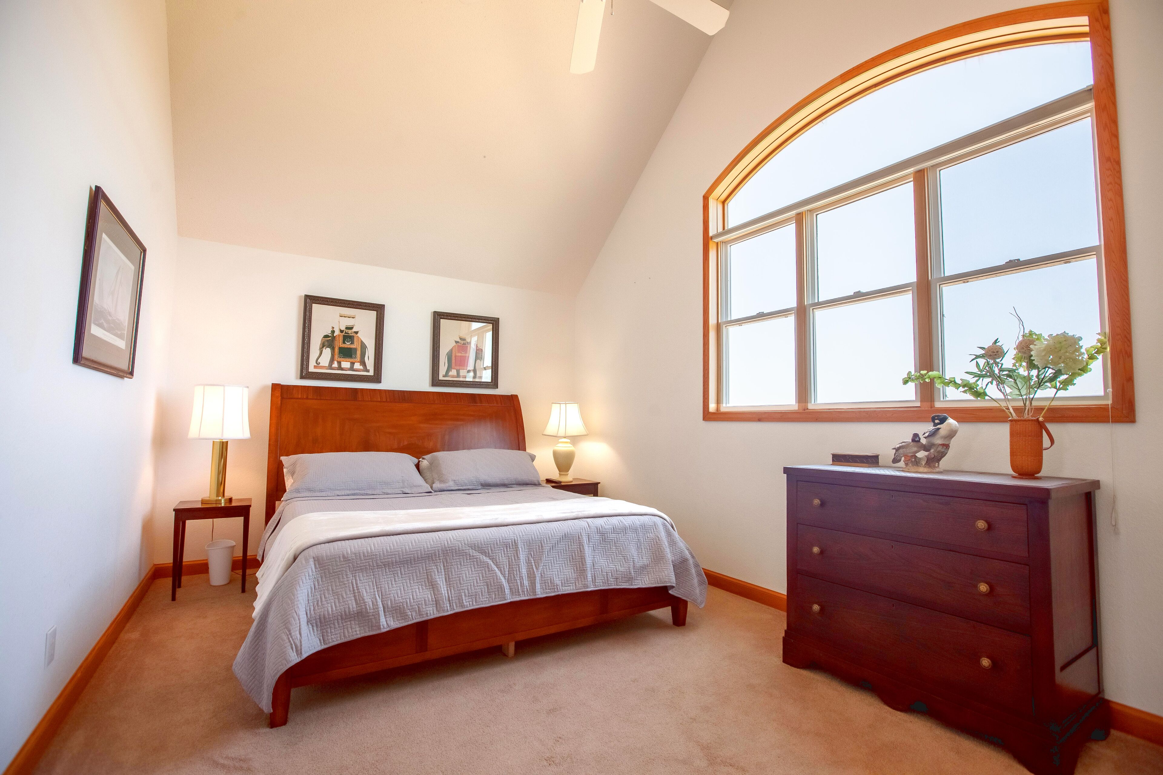 A bedroom with a wooden bed, two bedside tables with lamps, a dresser, and a large window with a view.