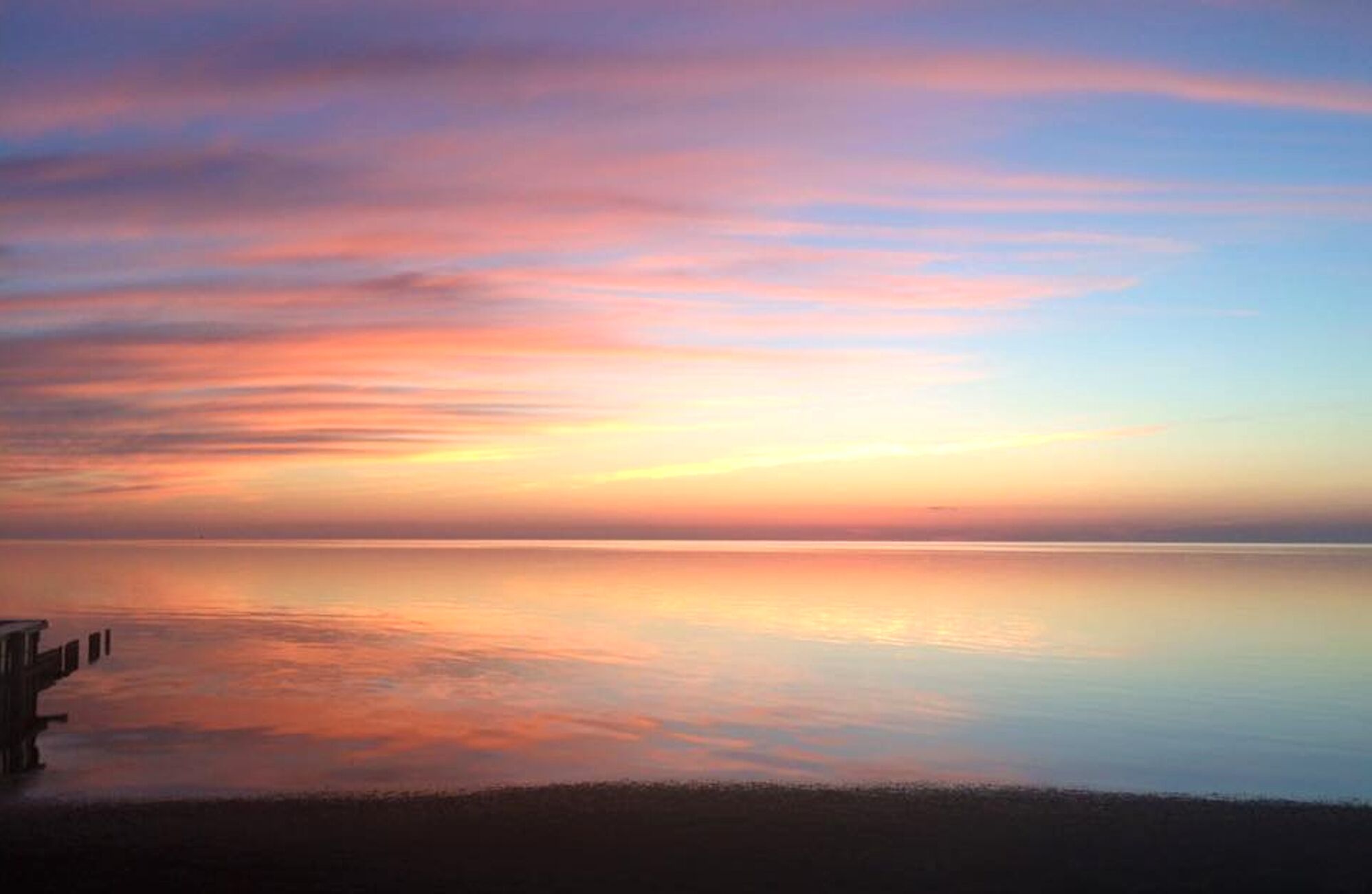 A calm sea at sunset with a pier extending into the water.