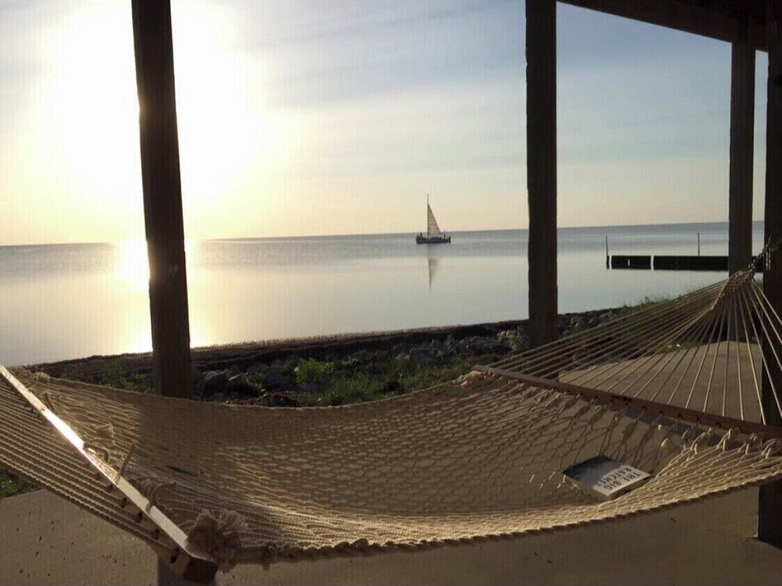 Eine Hängematte unter einer Holzkonstruktion mit Blick auf das Meer und einem Segelboot in der Ferne.