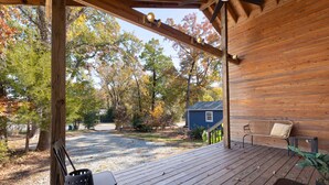 A wooden deck with a bench and a table, overlooking a driveway and a blue house surrounded by trees. - Modern, Quality 4BR Near Downtown (Durham)