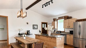 A modern kitchen with wooden cabinetry, a stainless steel refrigerator, a wooden dining table with chairs, and a hanging light fixture. - Modern, Quality 4BR Near Downtown (Durham)