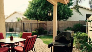 Eine Terrasse mit Grill, roten Sitzmöglichkeiten, einem Tisch und einem Pool im Hintergrund.